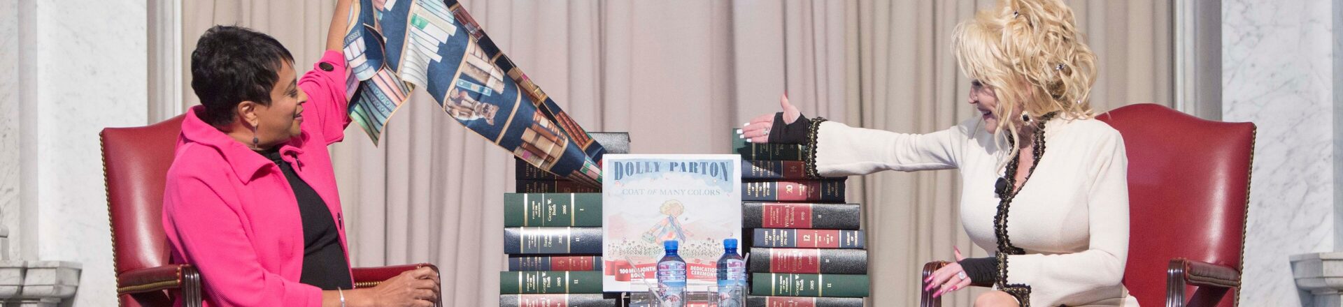 Librarian of Congress Carla Hayden and Dolly Parton unveil "Coat of Many Colors," the one hundred millionth book donated by Parton's nonprofit Imagination Library, during a ceremony in the Great Hall, February 27, 2018. Photo by Shawn Miller.